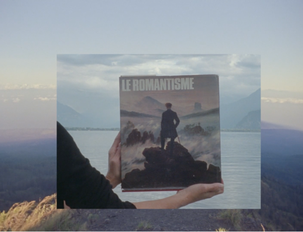 A film still showing two hands holding a book titled 'le romantisme' over the ocean