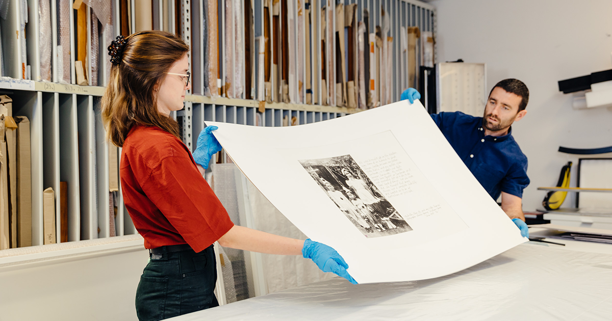 Two people handling an artwork in a storage room