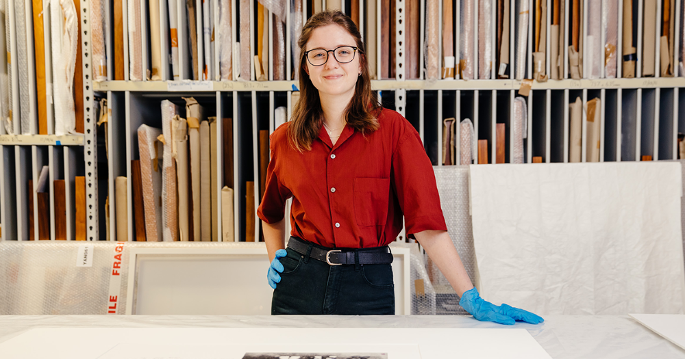 Registration intern, Chloe, wearing gloves at a worktable in front of art storage shelves