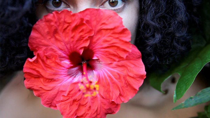 a film still showing a person staring into the camera with a hibiscus flower in her mouth 