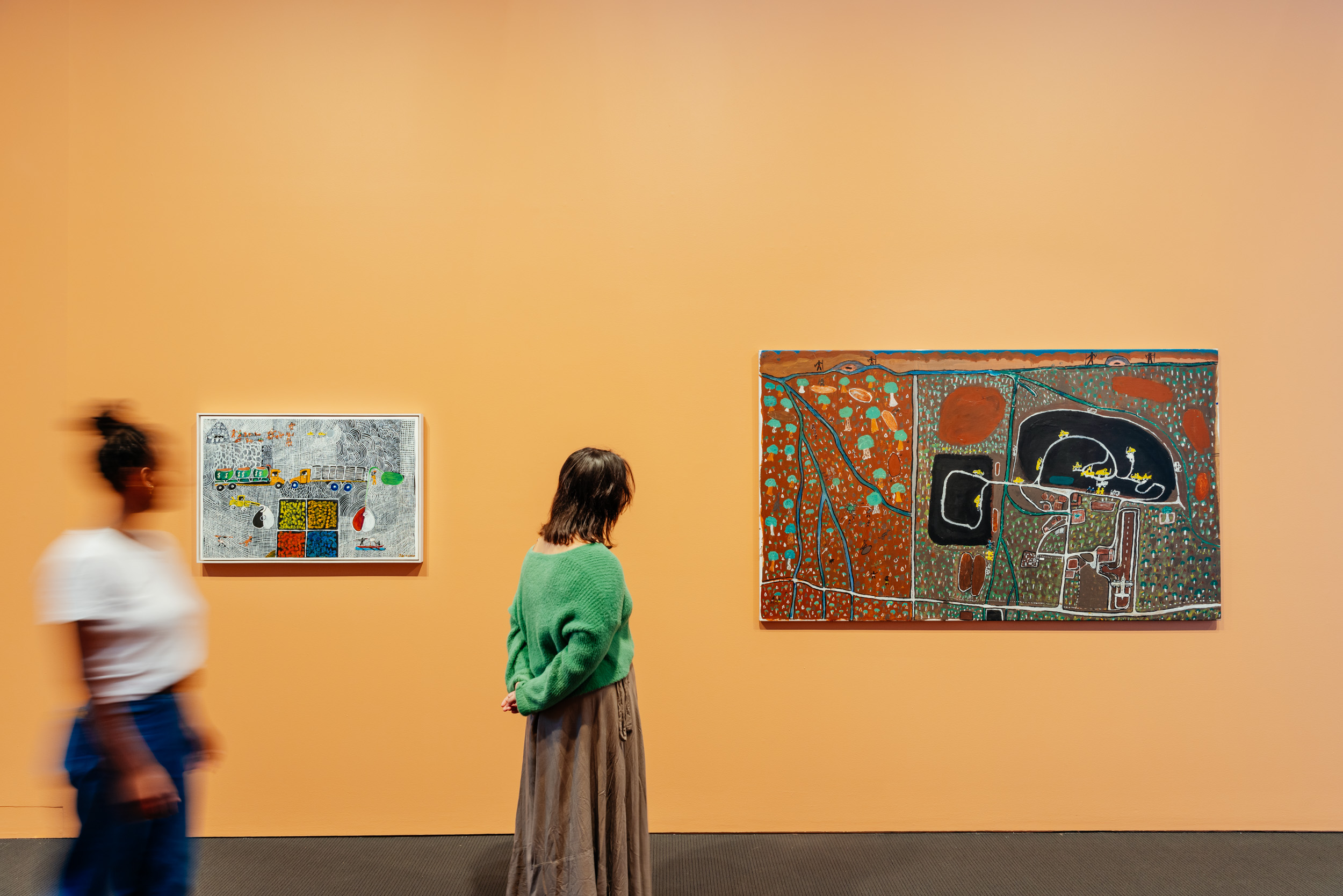 Two people viewing paintings that are hanging on a gallery wall