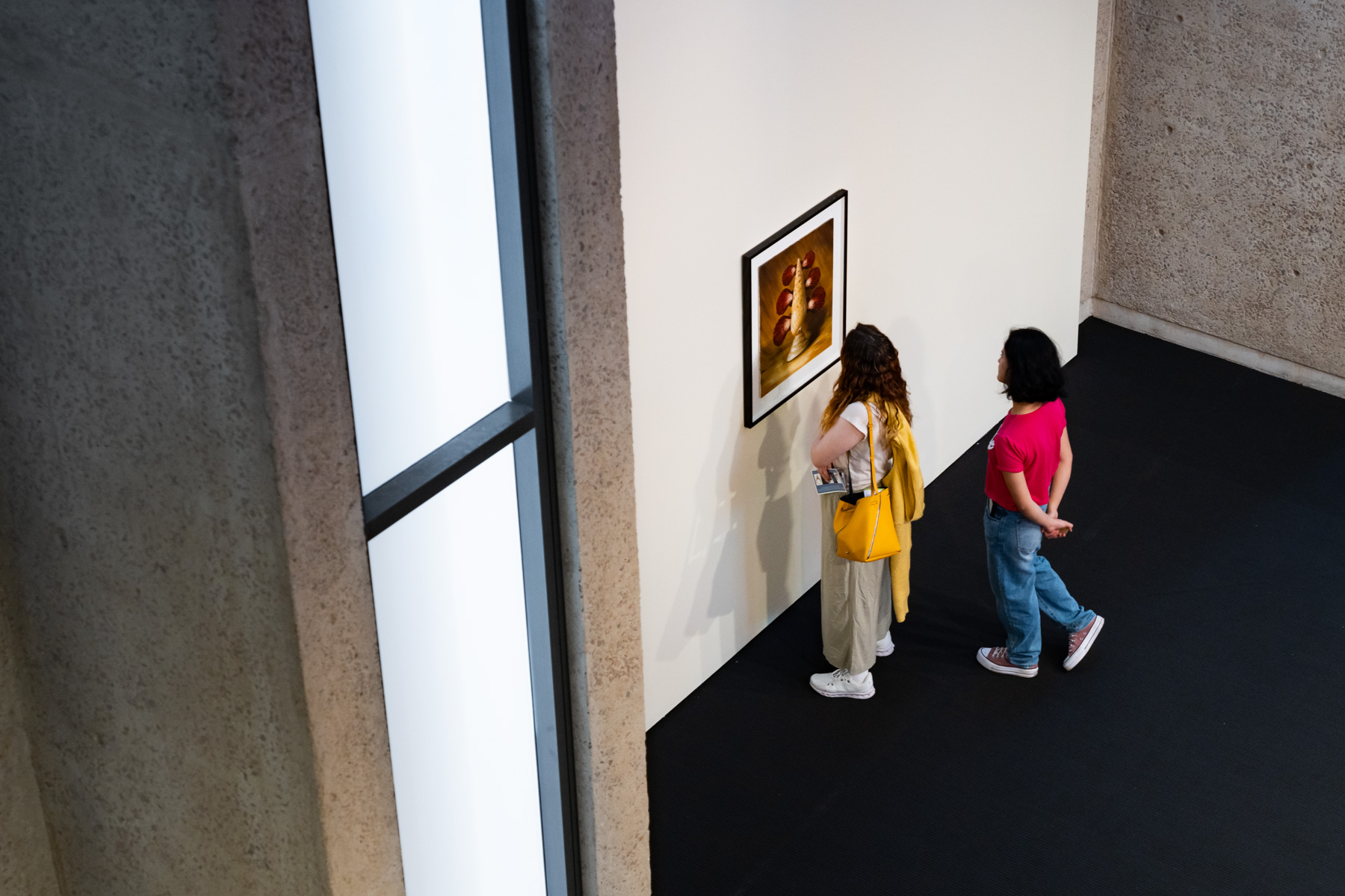 Two people viewed from above look at an artwork in a gallery space