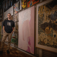 A person stands in front of a wall of artworks