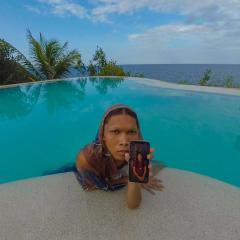 An image of a person in a tropical pool leaning on the pool step and showing their phone to the viewer.