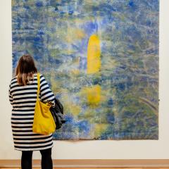A person views a painting by Judy Watson