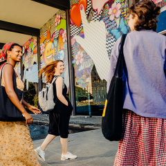 Three people walking towards a colourful building, the UQ Art Museum.