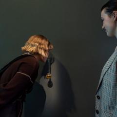 A visitor smelling a glass vile with a yellow liquid in it. Another visitor looks on.